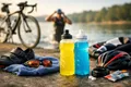 Bouteilles de boissons isotoniques posées près d'un lac avec du matériel de triathlon, illustrant l'hydratation pendant l'effort